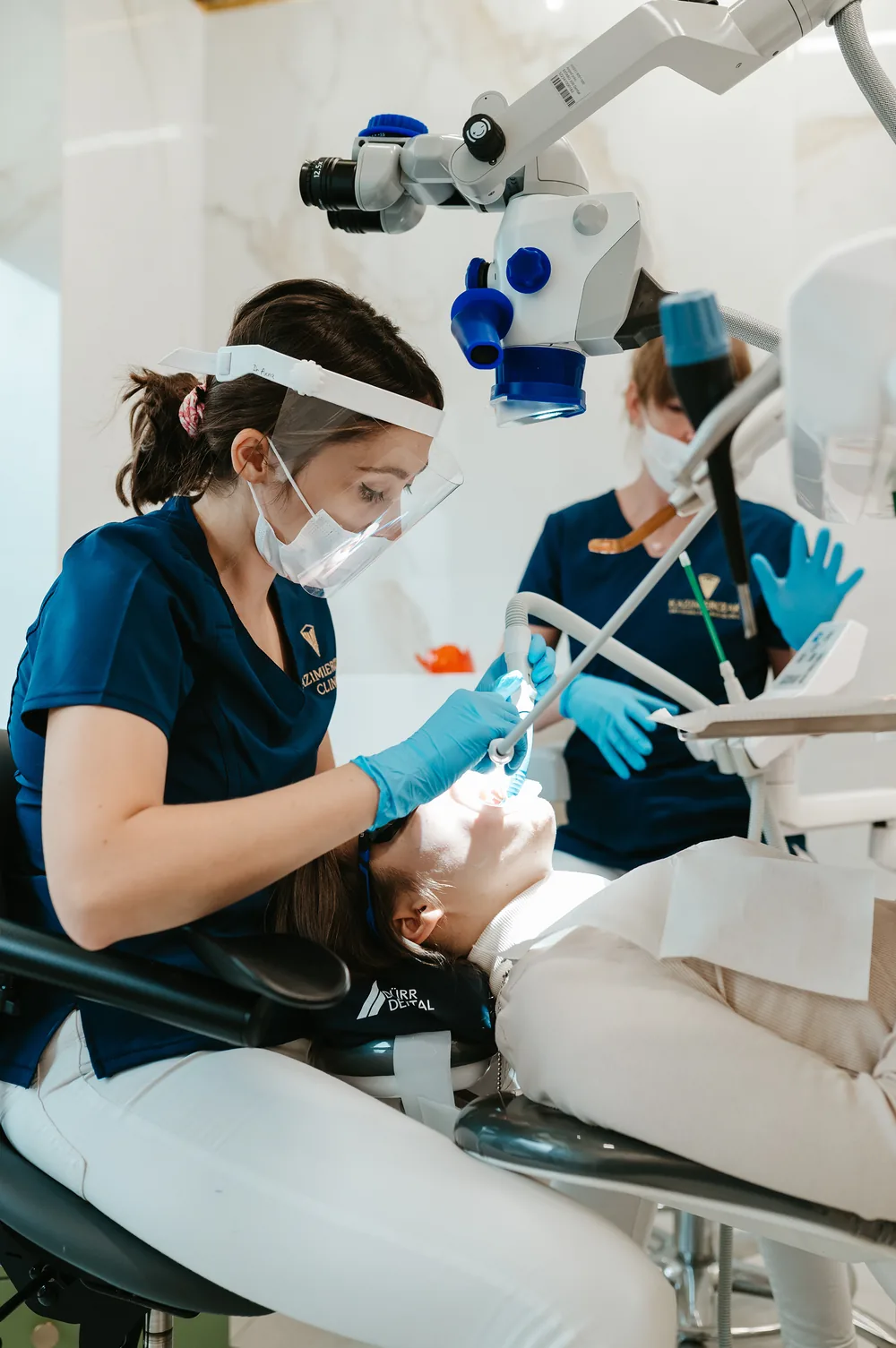 Lekarka Kazimierczak Clinic leczy pacjentkę pod mikroskopem z pomocą asystentki